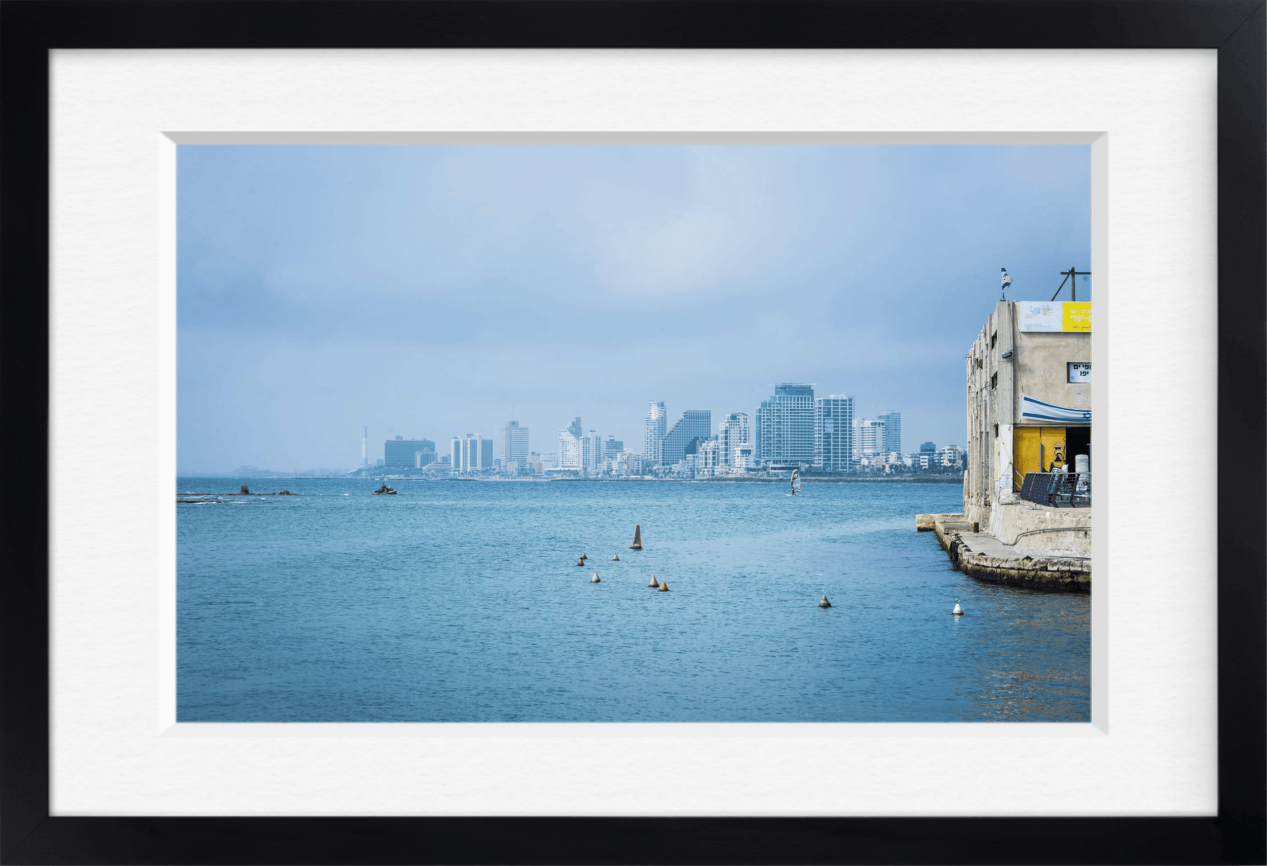 Framed archival print of a coastal city skyline across blue water with buoys and a stone jetty