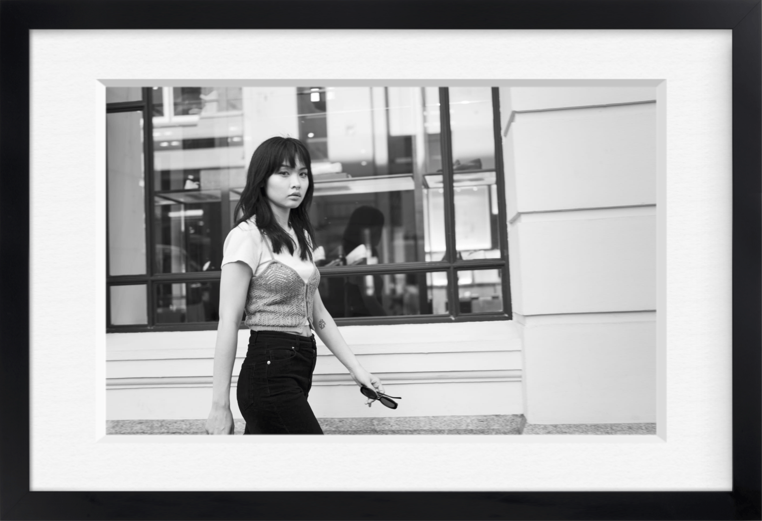 Black and white framed archival print of a young woman walking past shop windows