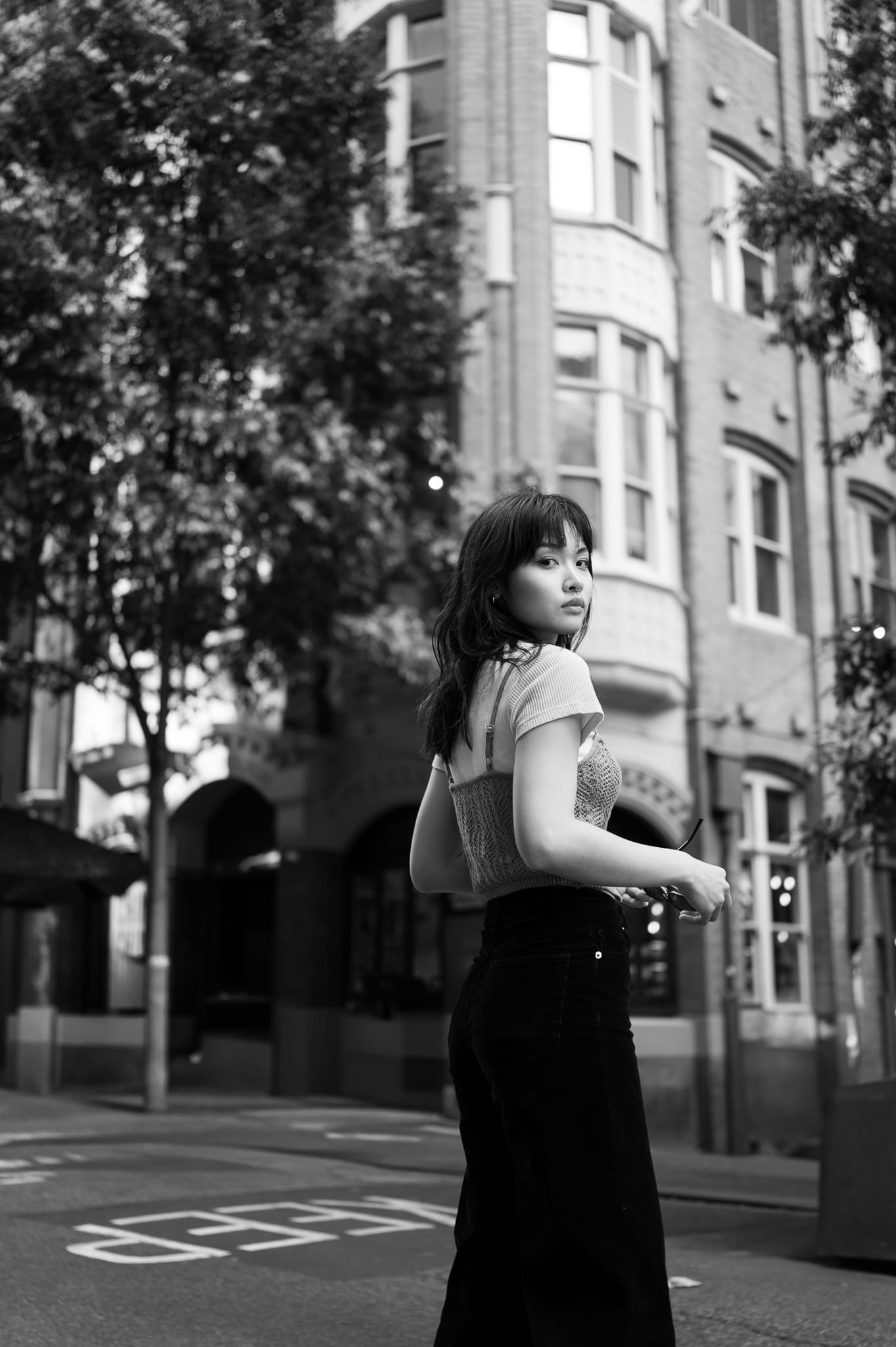 Editorial black and white street portrait of a young Asian woman looking back over her shoulder on a Melbourne heritage streetscape, shot on Leica Q3 — Arnold Szmerling Visual Legacy Artist