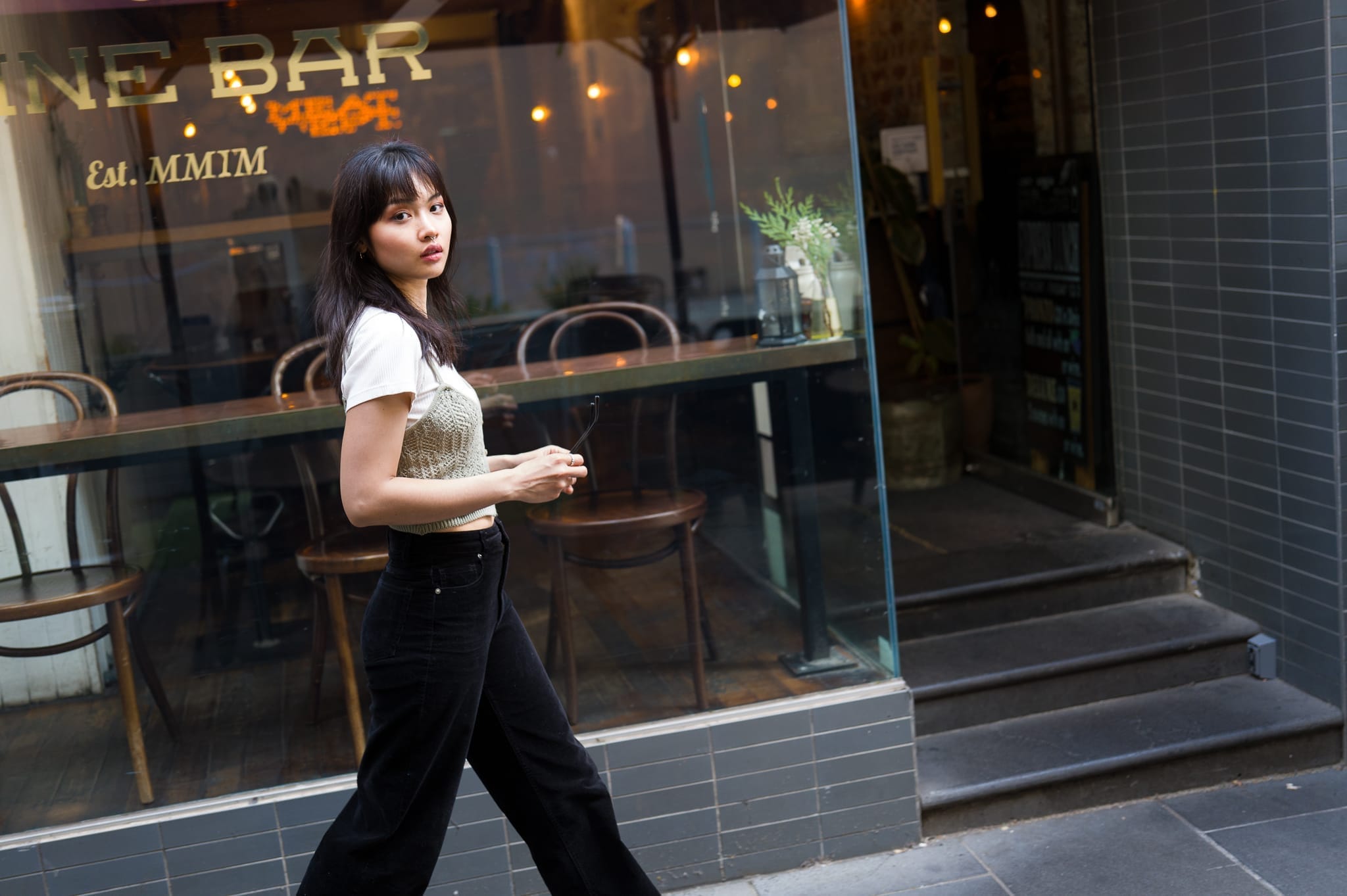 Walking in front of the wine bar Flinders Lane holding glasses and looking back at the camera with model Kobo, captured with the Leica Q3 43, a work of passion by Arnold Szmerling for the Visual Life Collection focusing on lifestyle legacy portraiture.