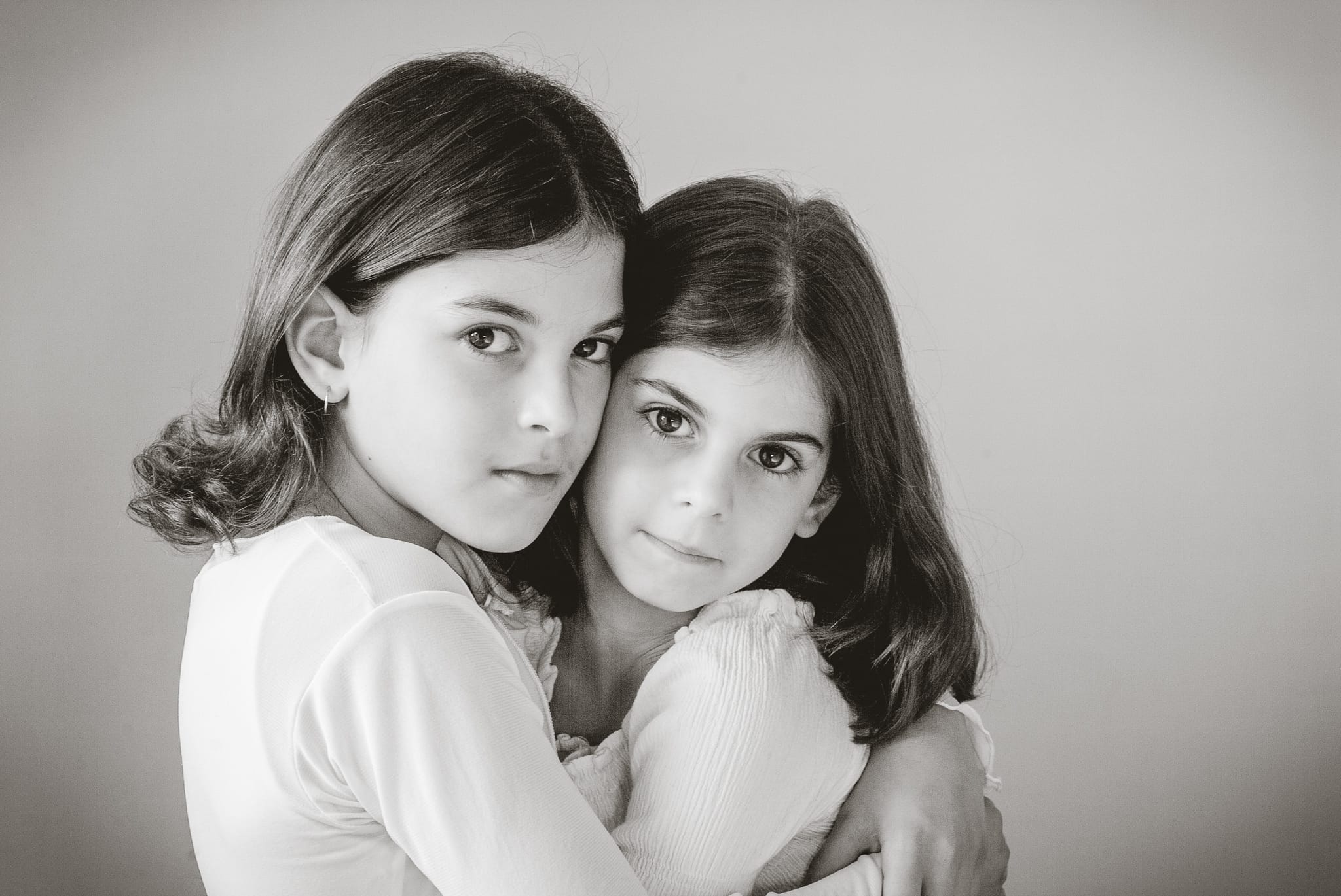 Two young sisters in a close embrace, heads resting together, both looking calmly into the camera with quiet presence. Black and white portrait by Arnold Szmerling.