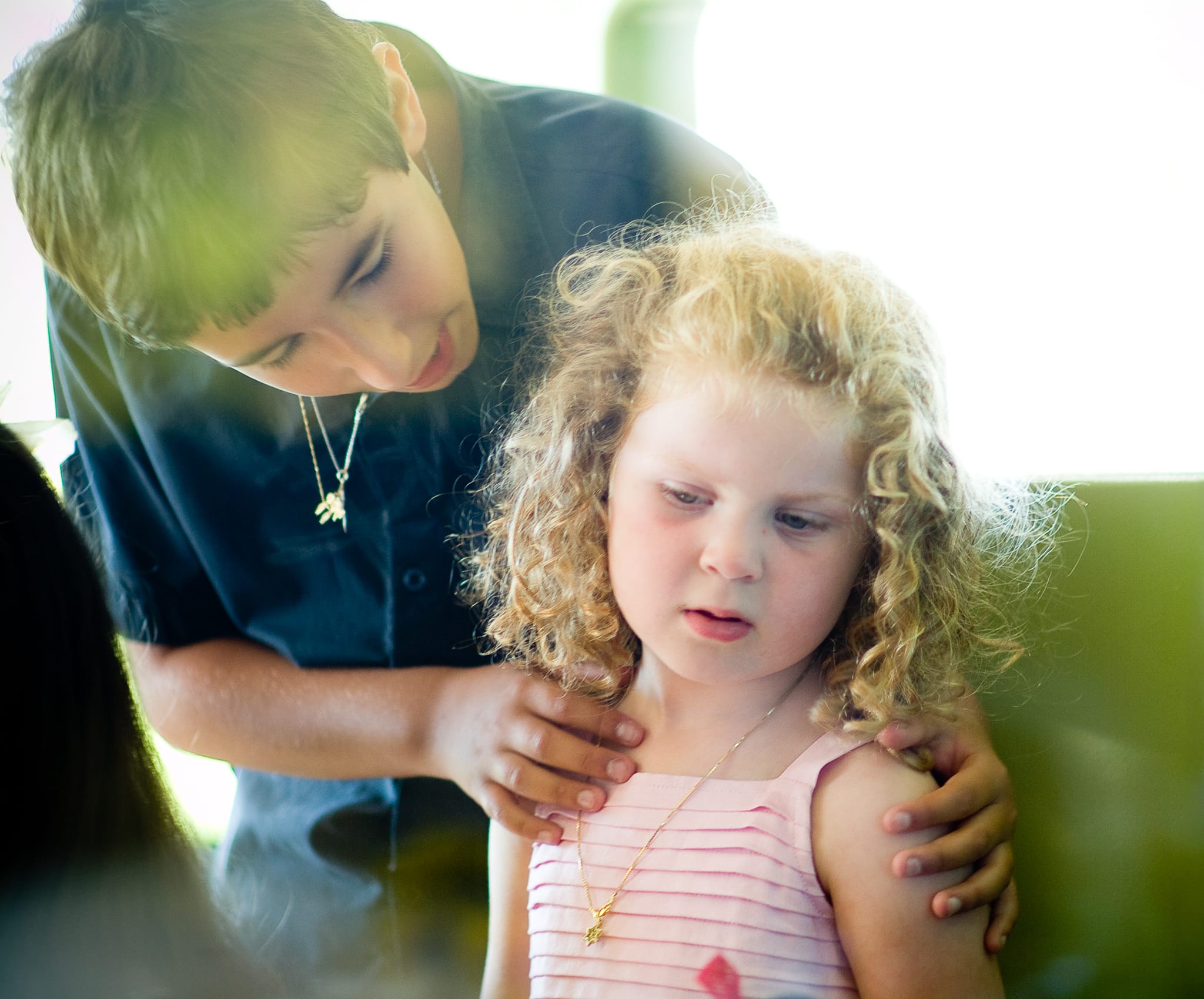 An older brother gently placing his hand on his younger sister's shoulder in warm backlit light — Arnold Szmerling Visual Legacy Artist