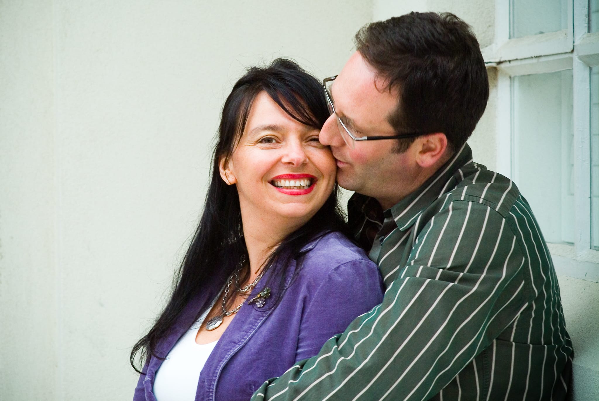 A couple sharing a joyful moment, man kissing woman's cheek as she laughs with red lips — Arnold Szmerling Visual Legacy Artist