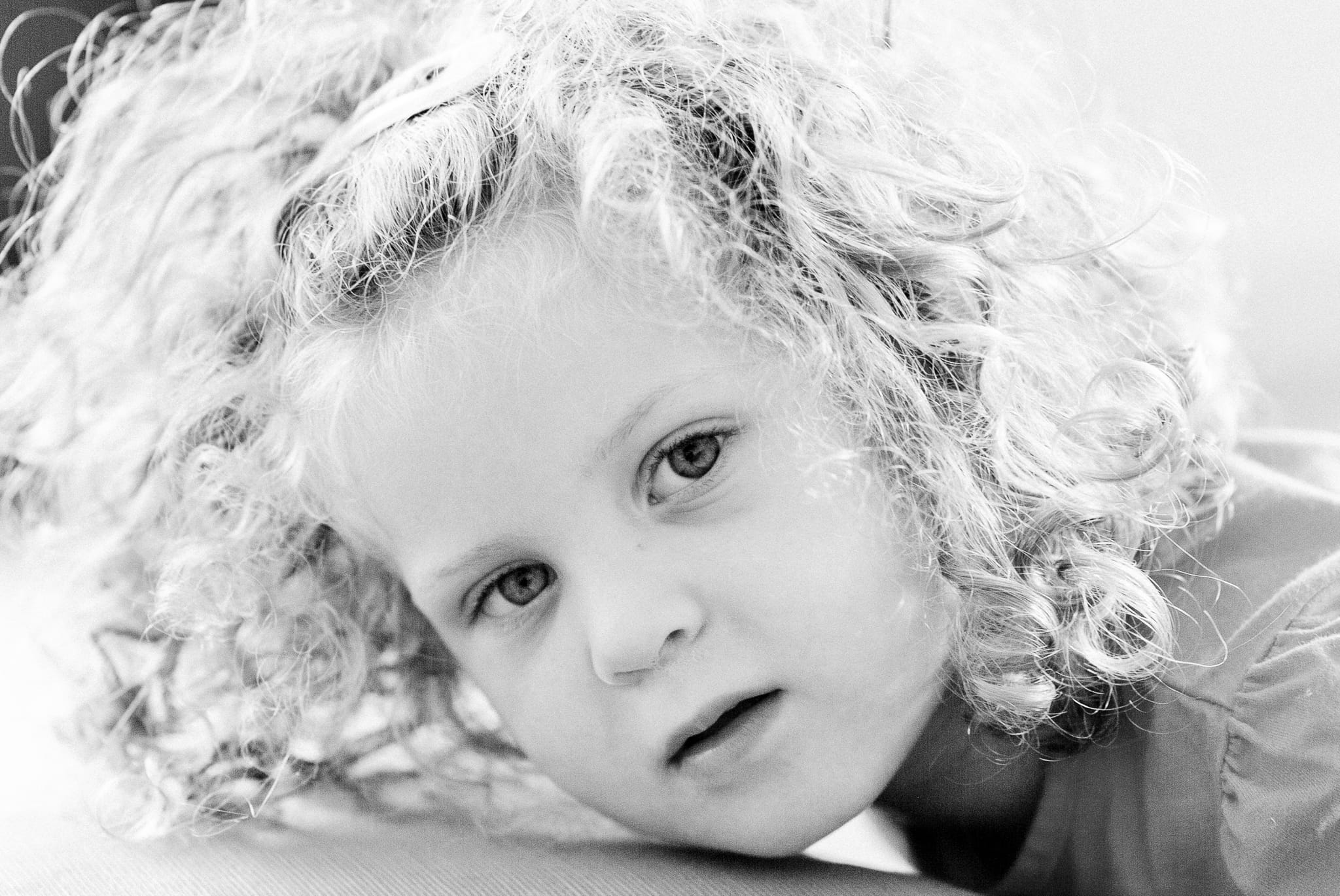 Black and white close-up portrait of a curly-haired young child resting her cheek, gazing sideways in natural light — Arnold Szmerling Visual Legacy Artist