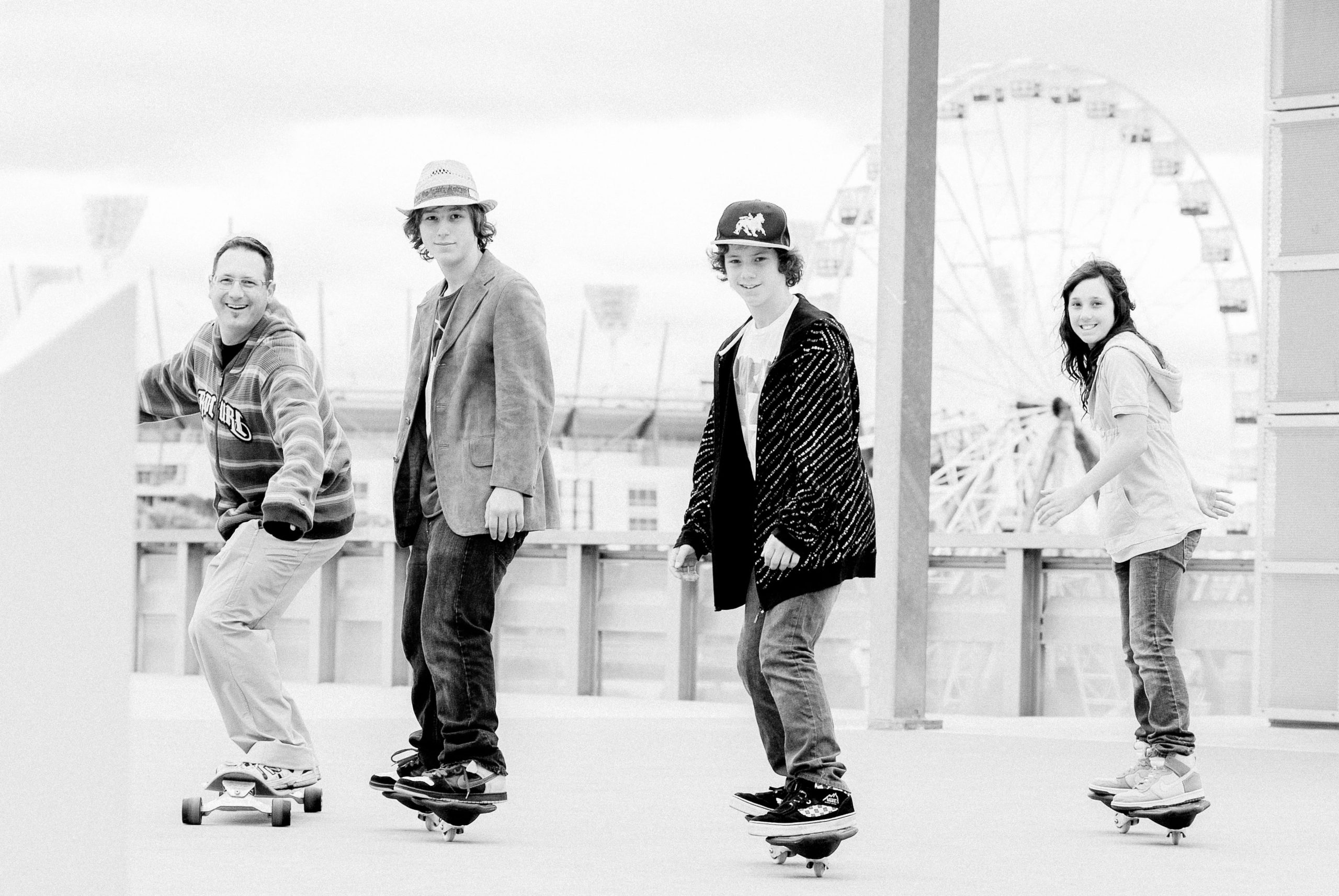 Black and white portrait of a father and three children skateboarding together on a Melbourne CBD rooftop with the MCG in the background — Arnold Szmerling Visual Legacy Artist