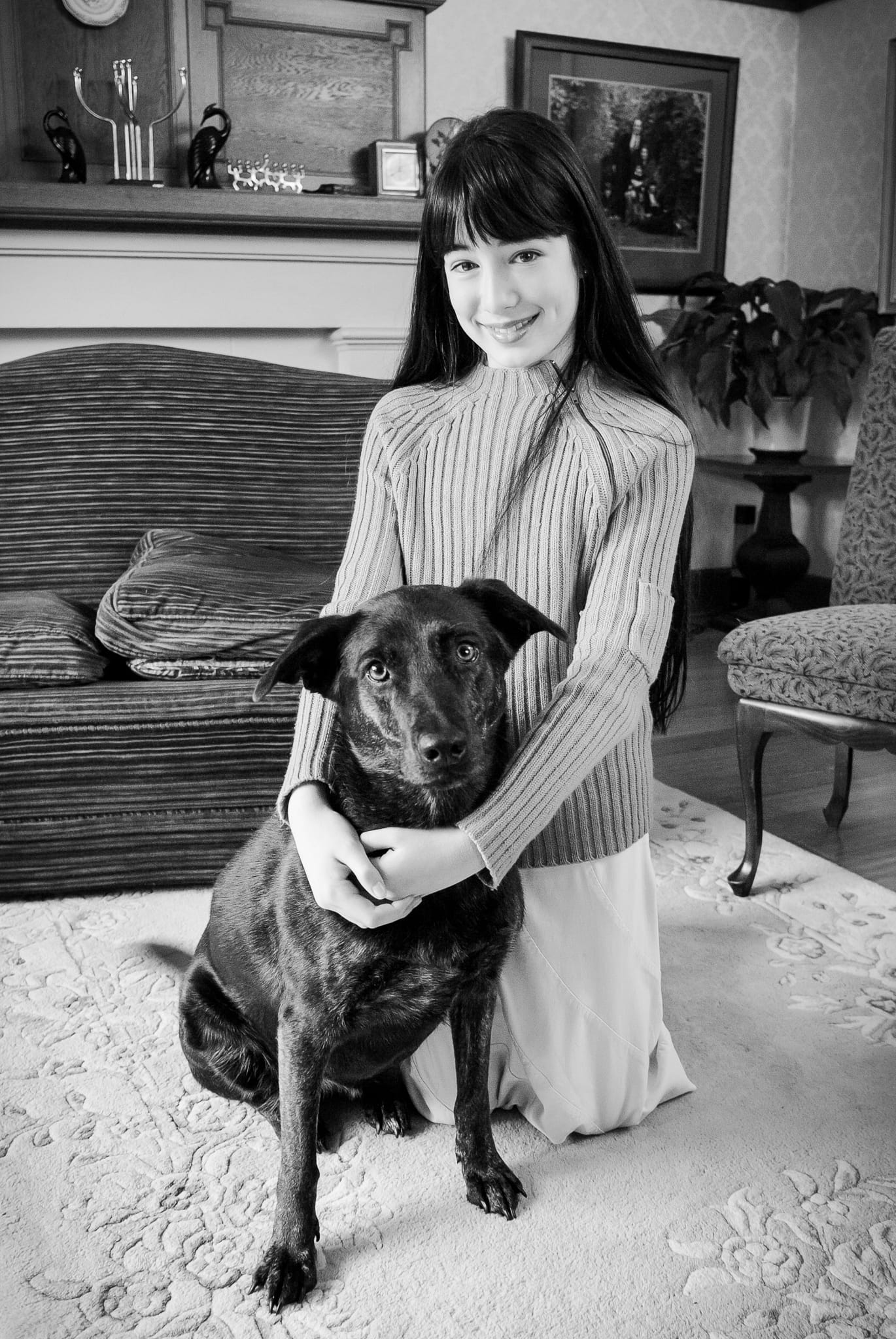 Black and white portrait of a young girl with her black labrador in the family living room — Arnold Szmerling Visual Legacy Artist