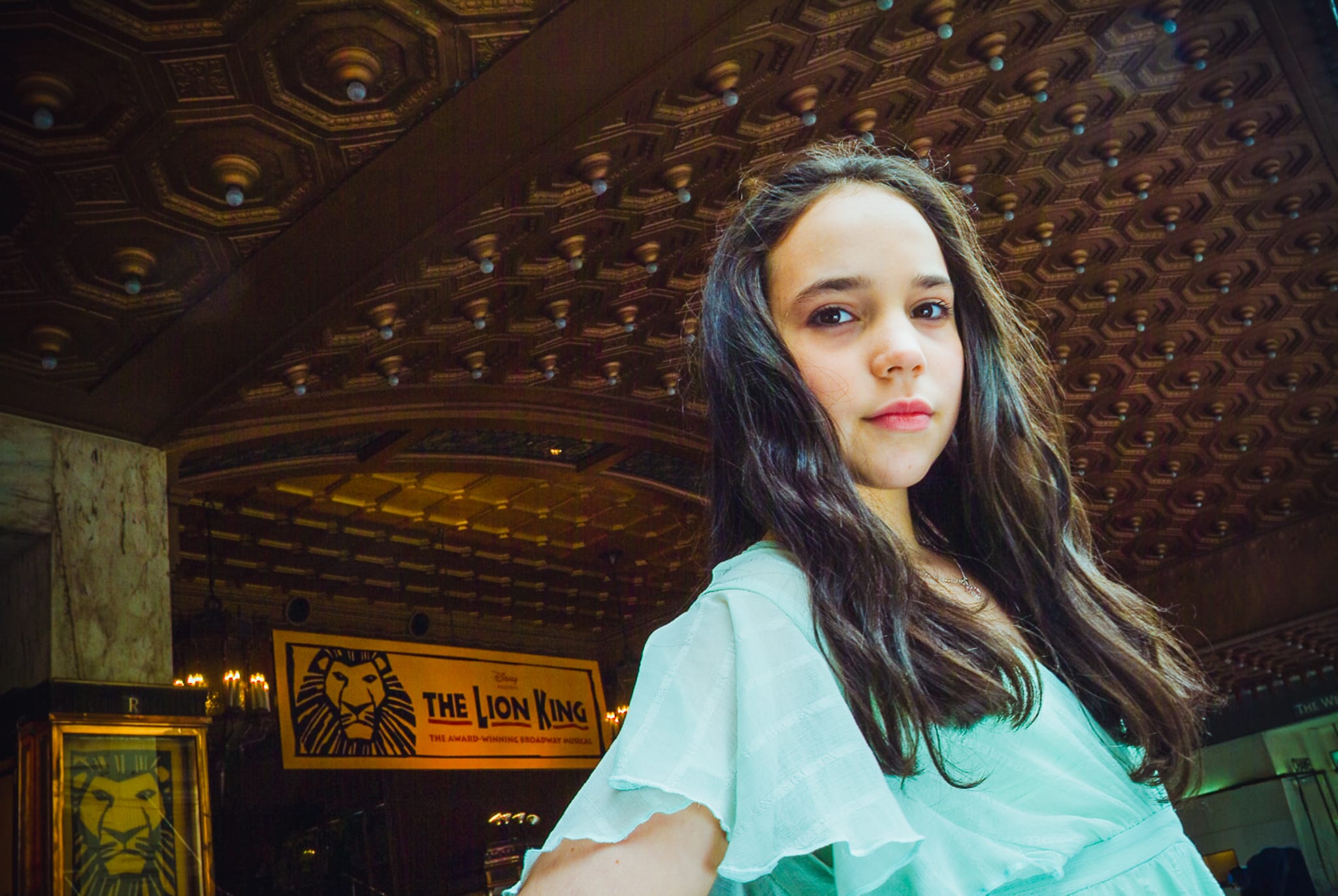 A young actress inside the Regent Theatre Melbourne with The Lion King signage and ornate ceiling — Arnold Szmerling Visual Legacy Artist