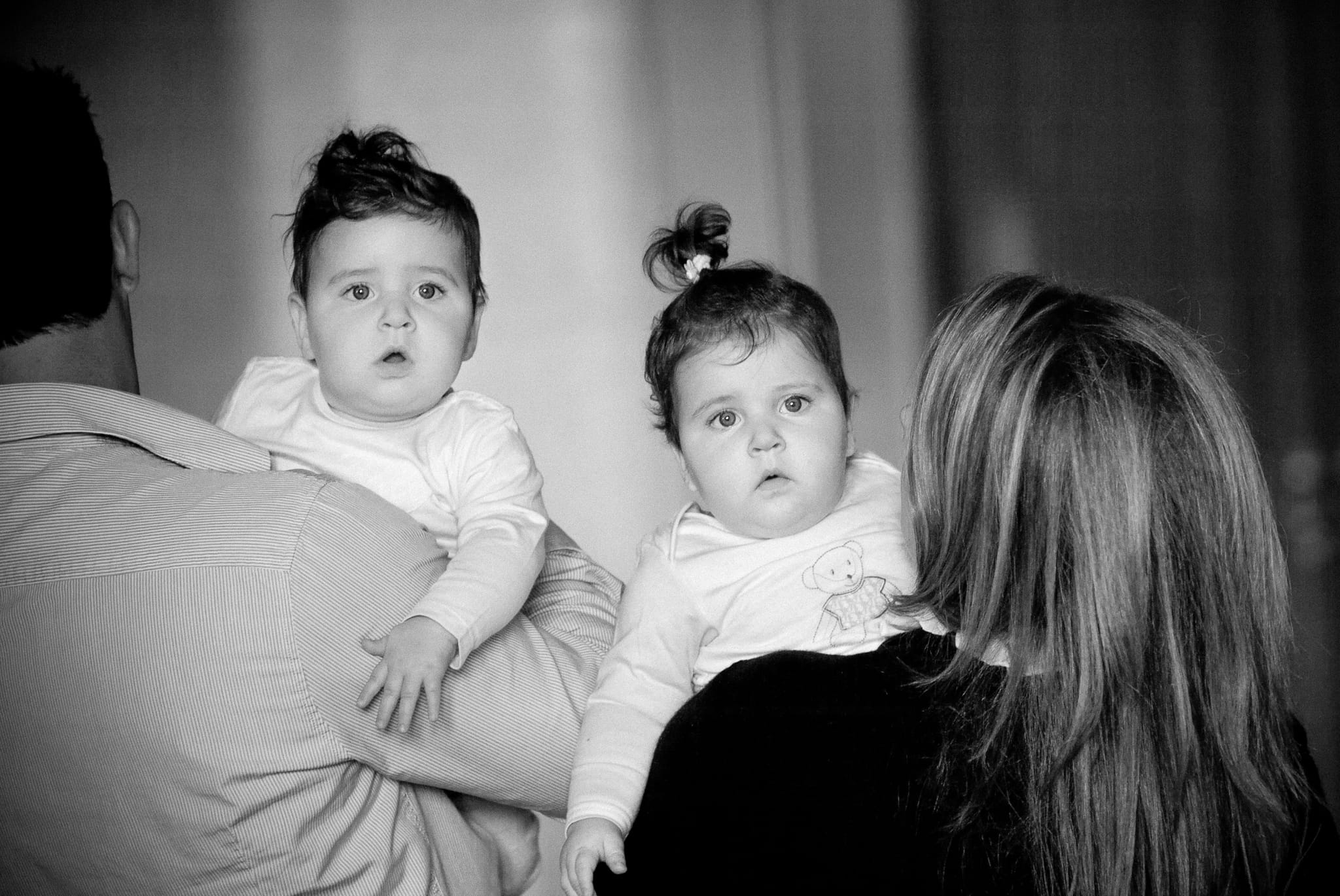 Black and white portrait of twin babies held by their parents, both gazing wide-eyed at the camera — Arnold Szmerling Visual Legacy Artist